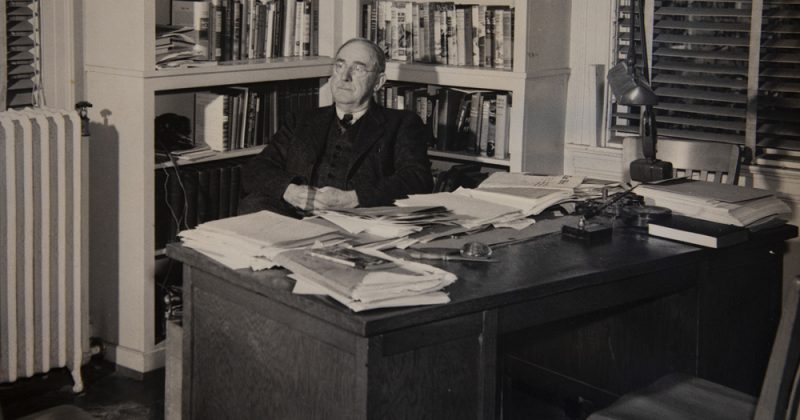 Howard Odum sits in his "famous" office in the UNC Alumni Building. Much like his home office, it was covered in books and papers that he didn't allow anyone to reorganize. Photo courtesy of University Archives.