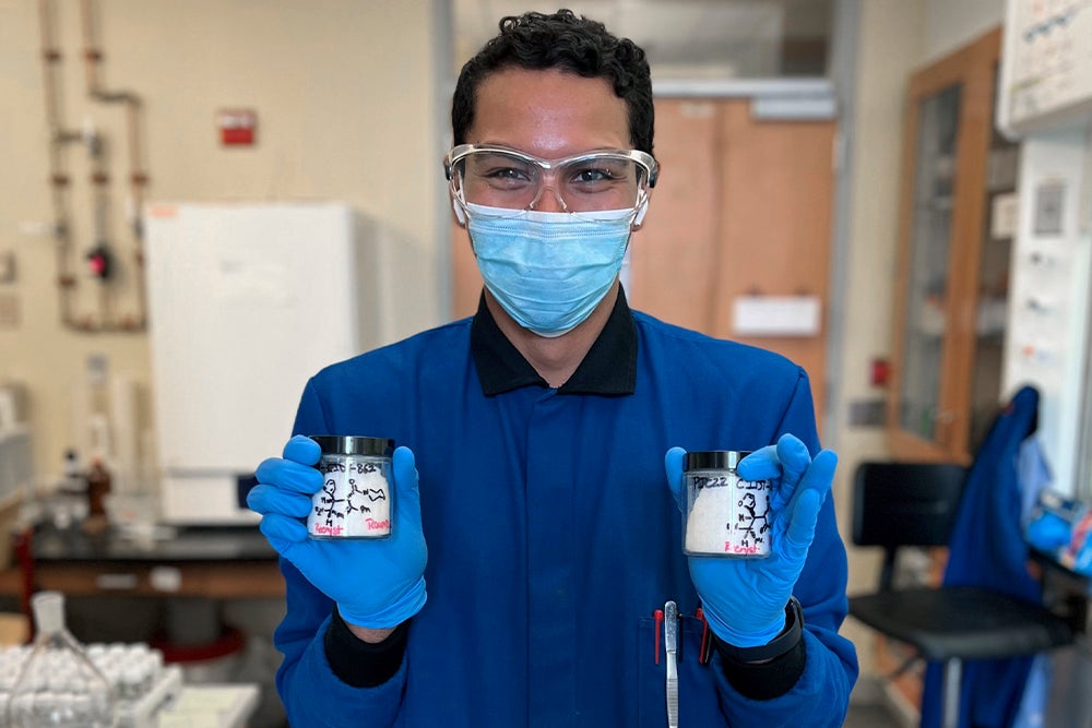 Pedro de Jesús Cruz in a research lab holding containers of solid compound produced in their study.