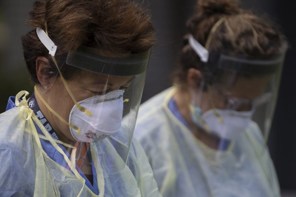 two health care workers wear masks and face shields while conducting a study on COVID-19