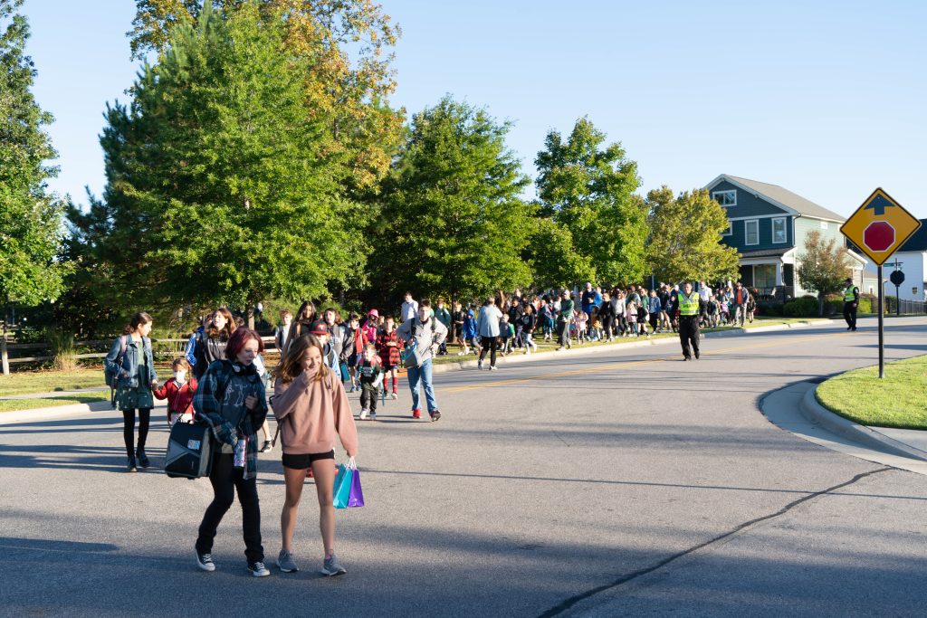 A long line of students with some parents walking down the sidewalk on their way to school.