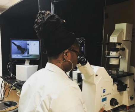 A woman in a lab coat looks into a large microscope.