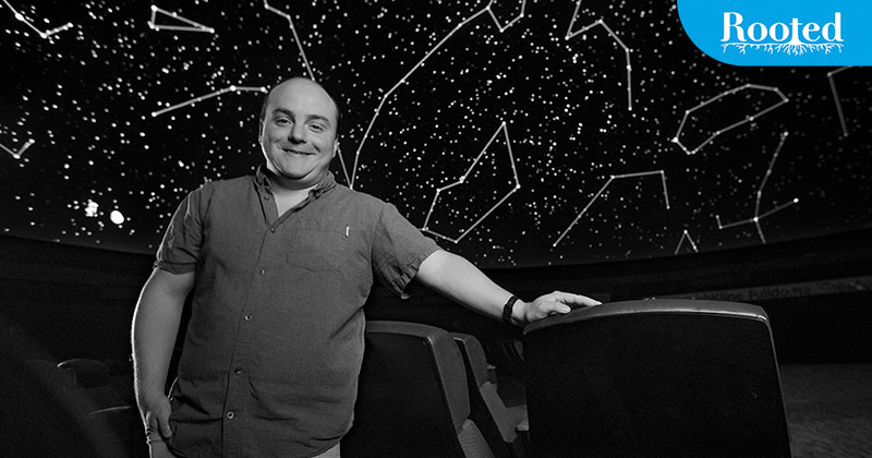 Nick Eakes standing in a planetarium theater with constellations projected on the screen above him.