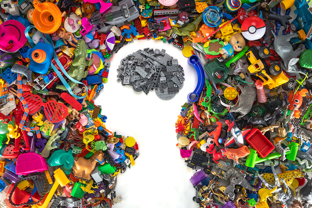 Plastic toys in various colors are arranged to form the shape of a child's head and shoulders, while gray toy building bricks are used to depict the child's brain.