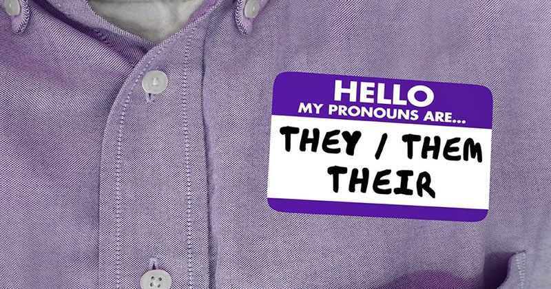 A close up of a name tag that says they/them/their on a purple shirt