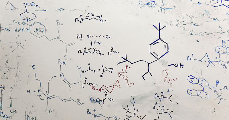 A white board with chemical structures written on it.