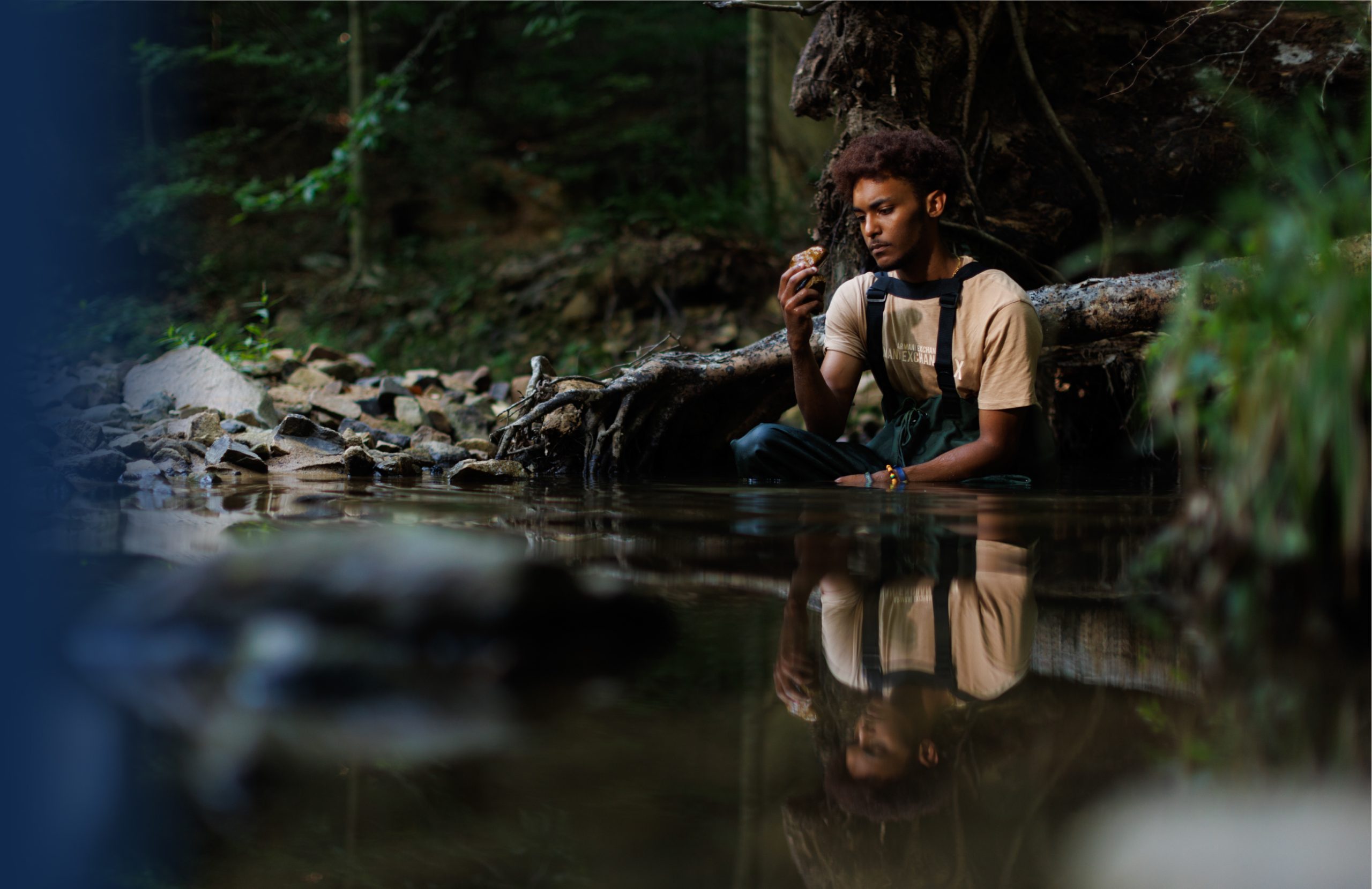 Photo of a researcher in a creek in weighters, looking at a rock.