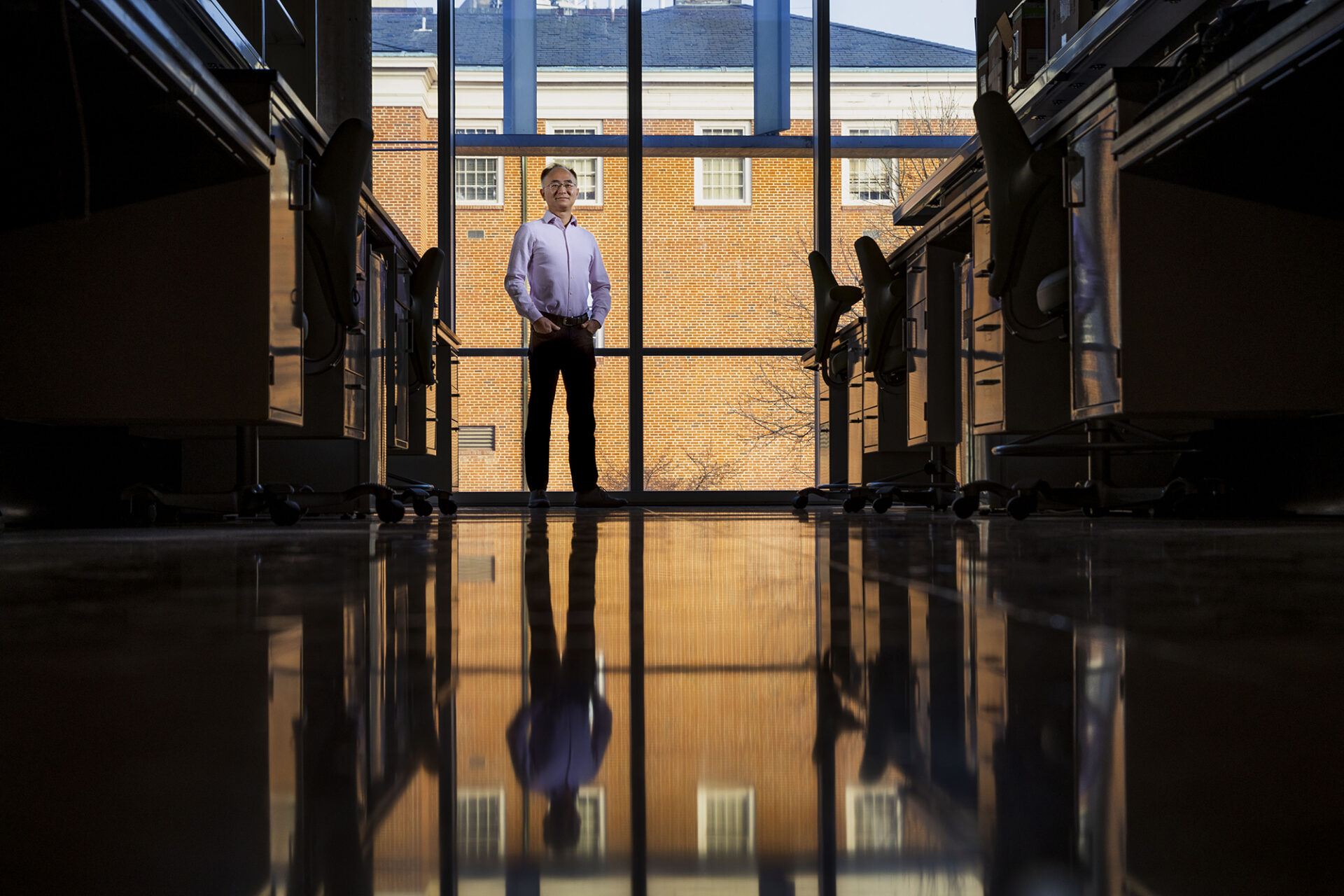 Wei You stands in a chemistry lab, and his reflection is mirrored on the shiny concrete floor.