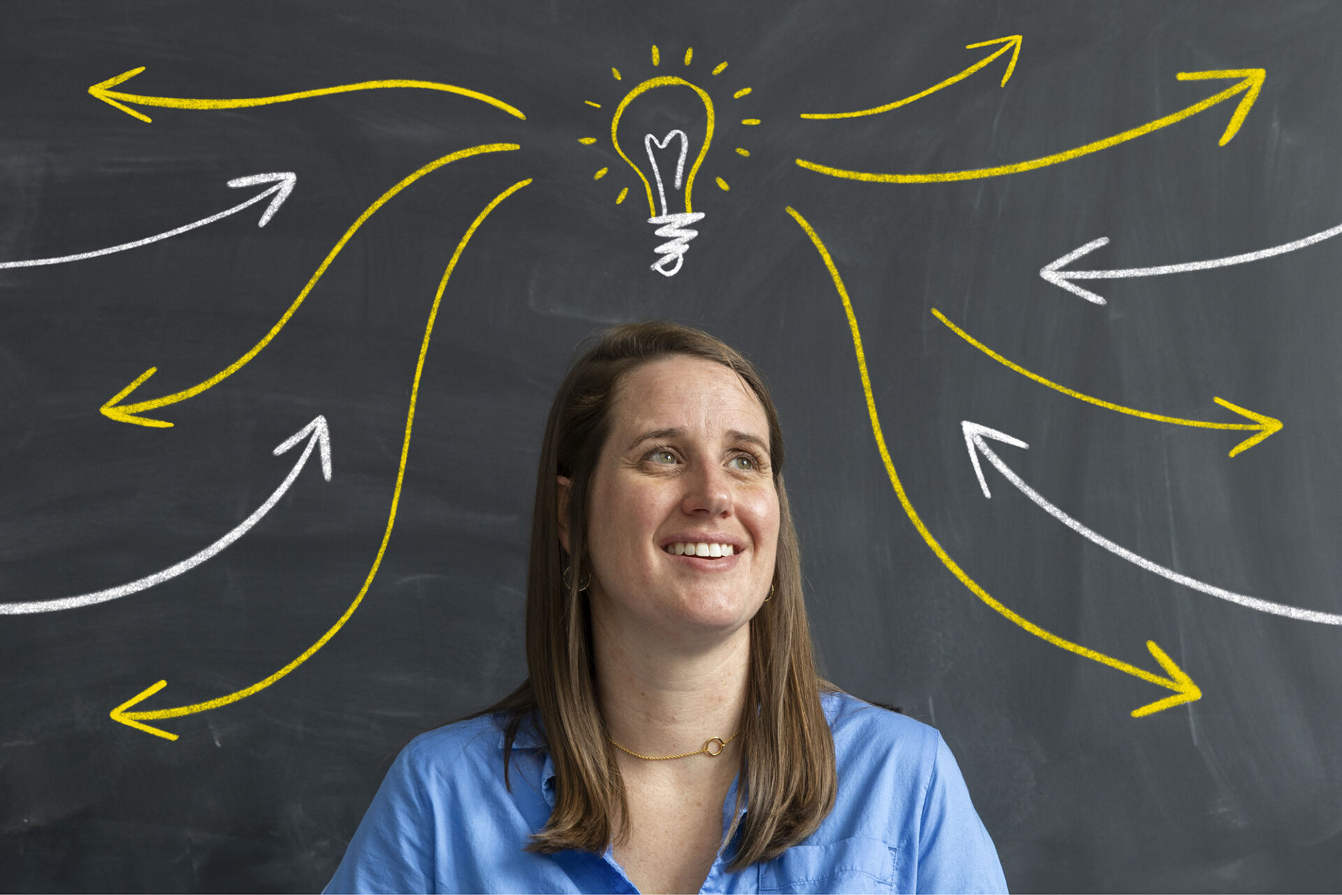 a woman in front of a blackboard with a drawing of a lightbulb with arrows going toward and away from it