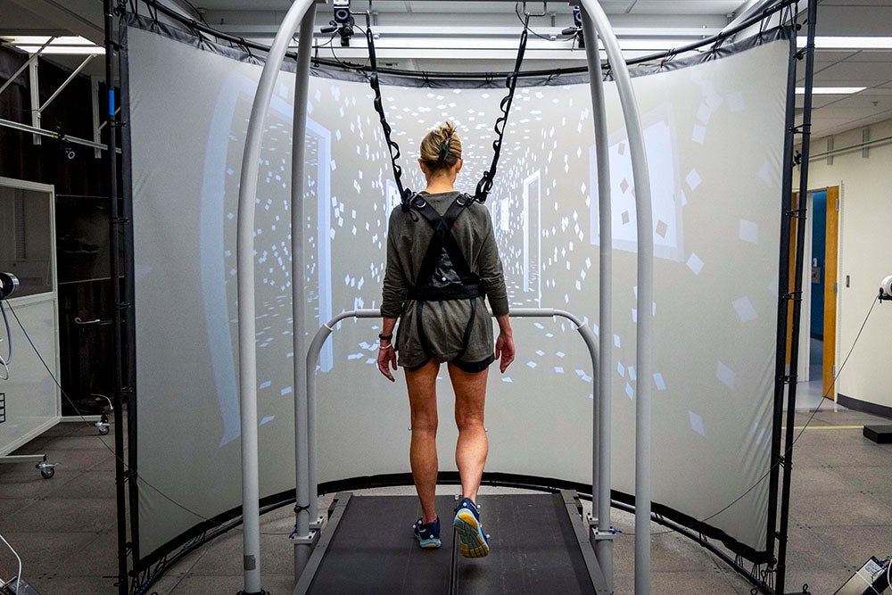 a woman in a harness walking on a treadmill in a lab