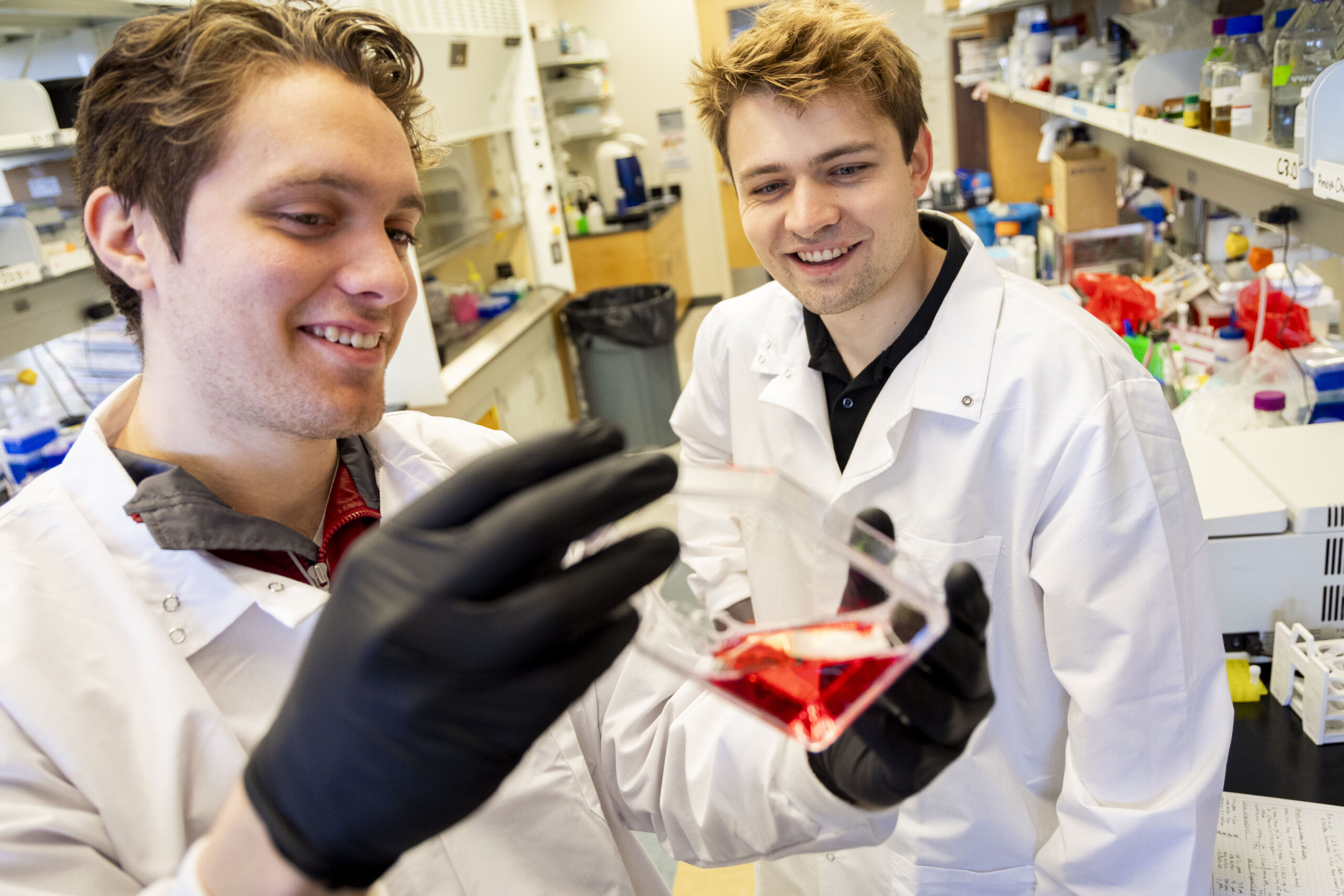 Two researchers smile at substance in a vial.