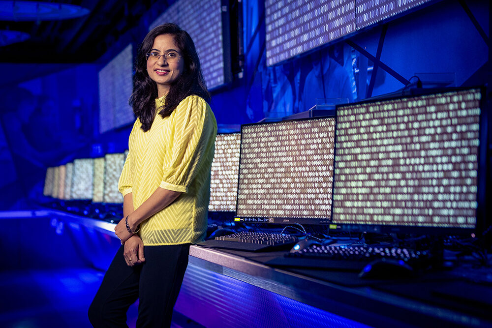 a woman in front of a line of computers covered in code.