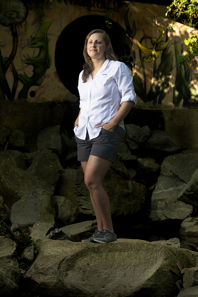 a woman stands in front of a sewer drain covered in graffiti 