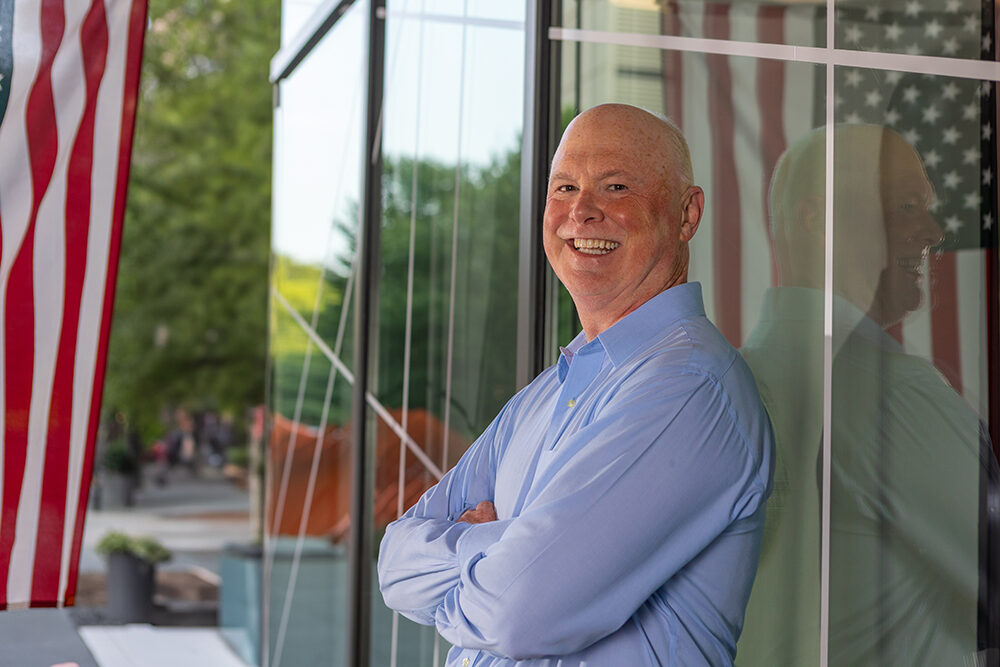 a man leans against a window with a reflection of an American flag in it