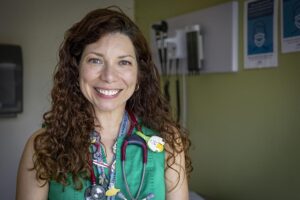 A female doctor smiles for a portrait in an exam room.