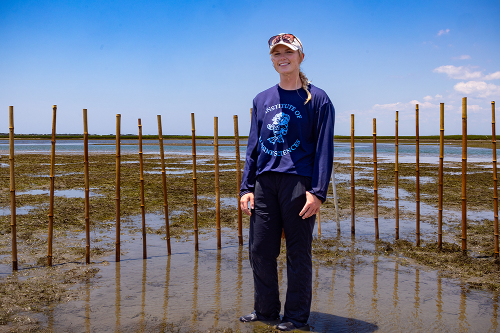 a young woman stands in front of wooden poles embedded in the seafloor