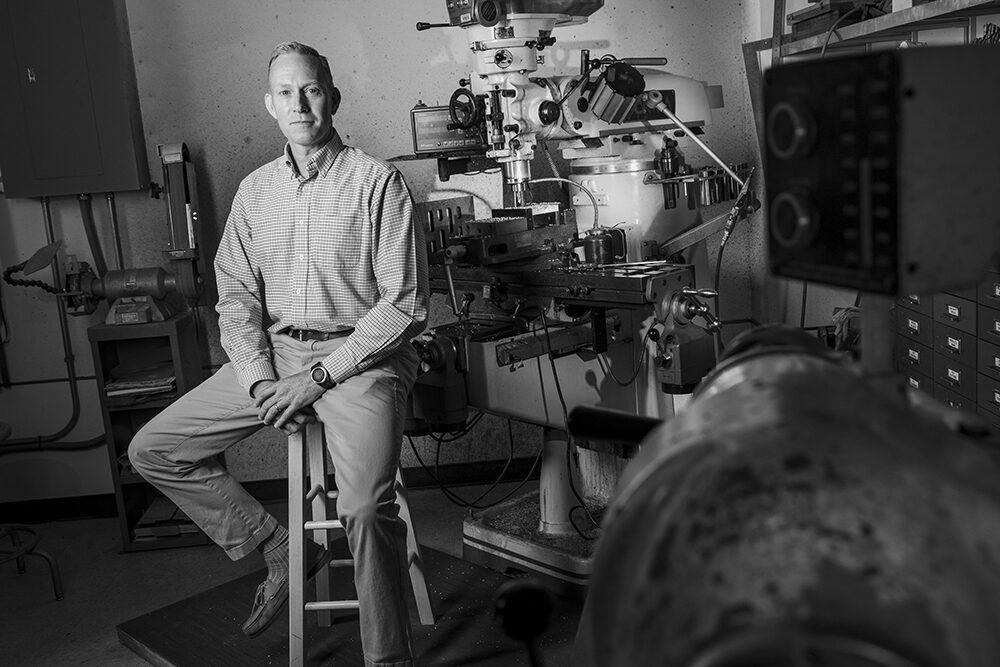 a man sits on a stool in a robotics lab