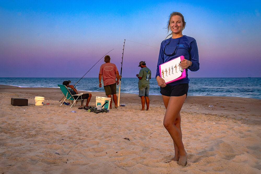 young woman on the beach at sunset with anglers fishing behind her.