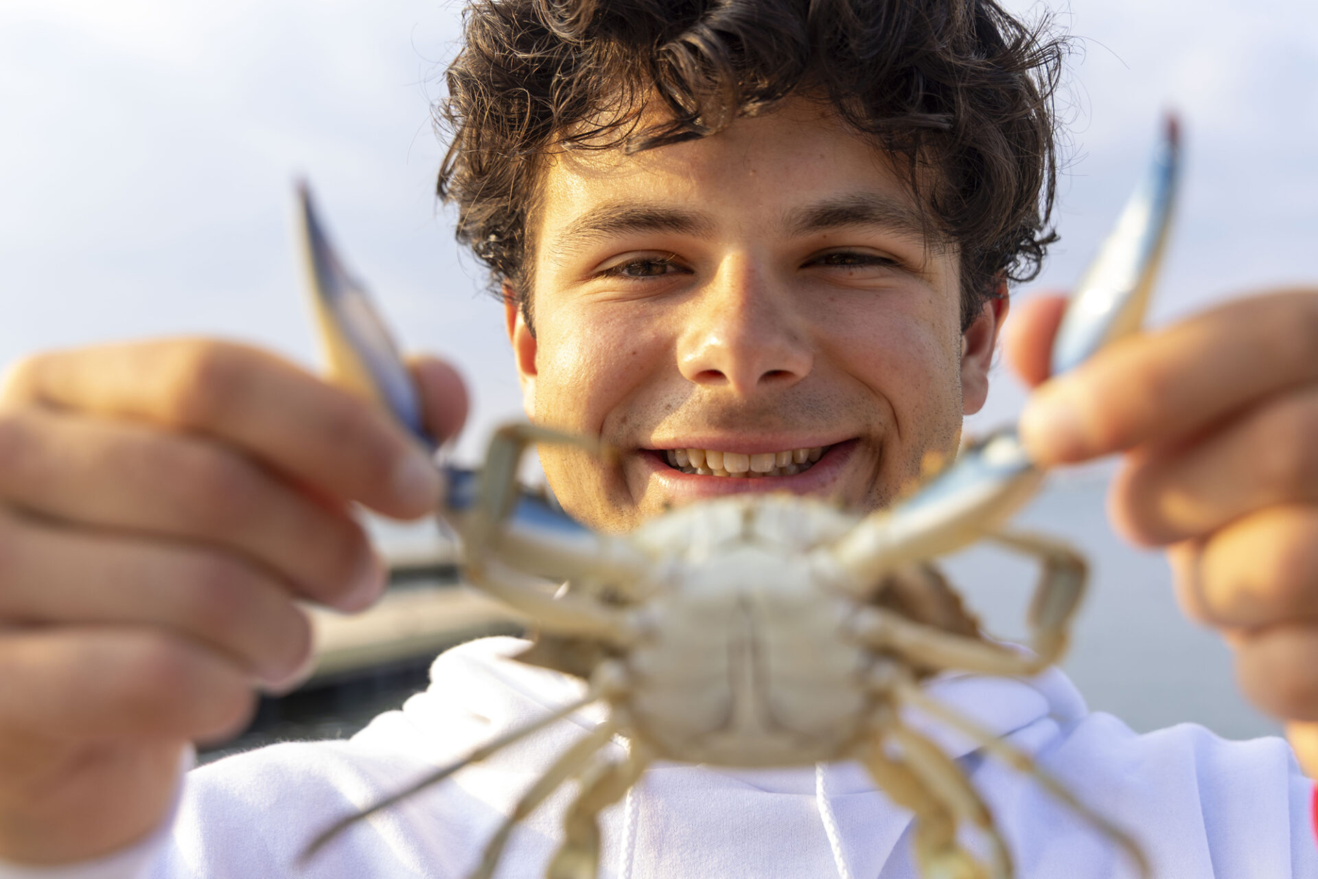 a young man holds up a blue crab