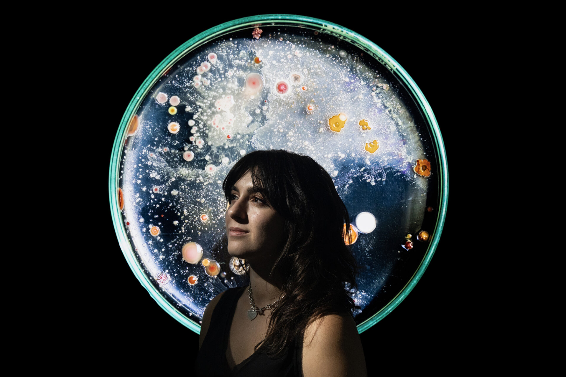 a young woman in front of an image of a petri dish covered in bacteria