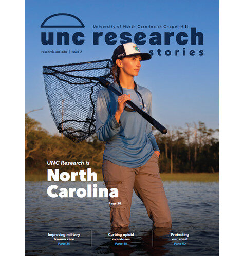 UNC Research Stories 2025-2026 magazine cover, featuring a photo of Institute of Marine Sciences researcher Alexis Longmire standing in knee-deep water in Bogue Sound. She carries a large fishing net.