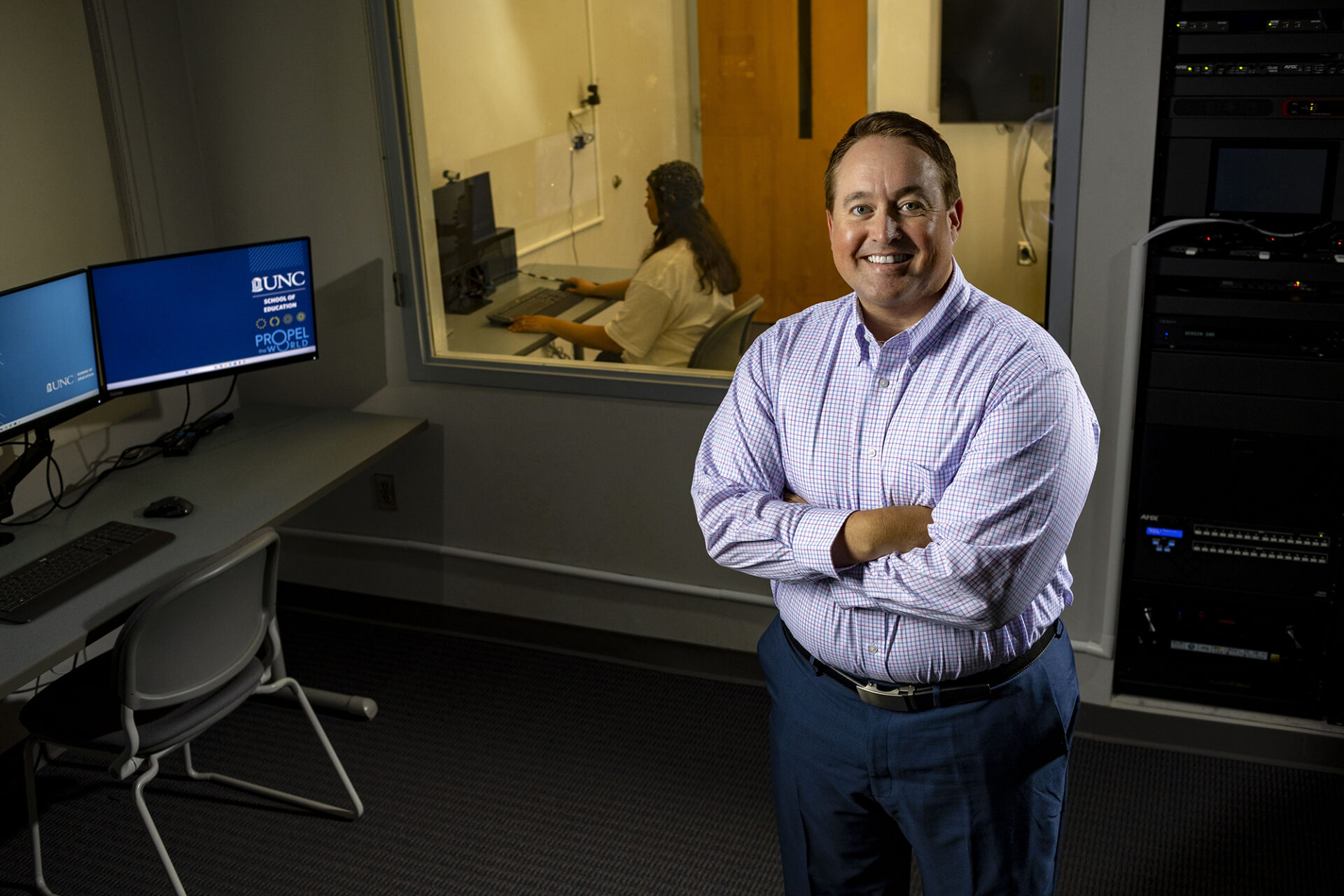 a man stands in his lab; a student wearing a cap that measures brain activity is behind him