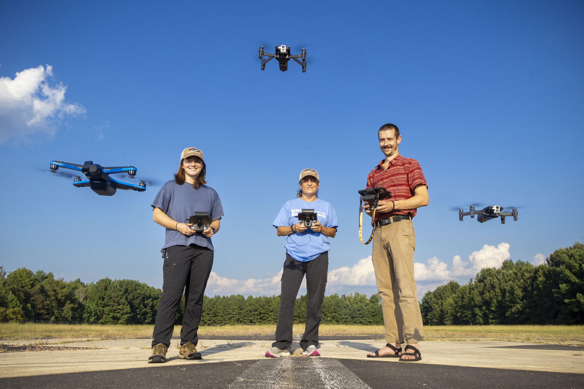 three researchers fly drones over a tarmac