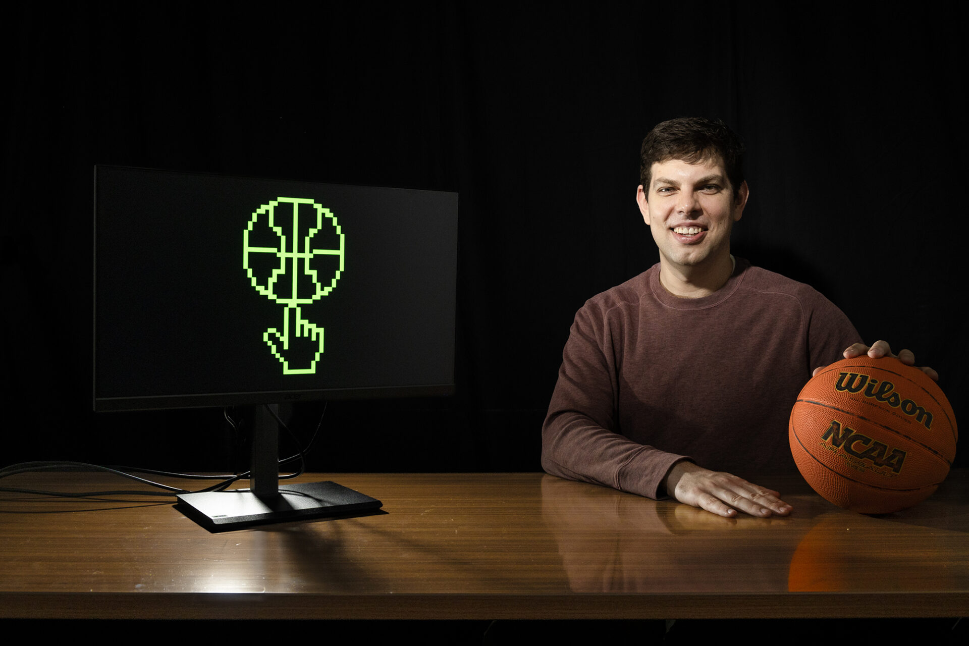 Gedas Bertasius next to a monitor with a green 8-bit basketball on it