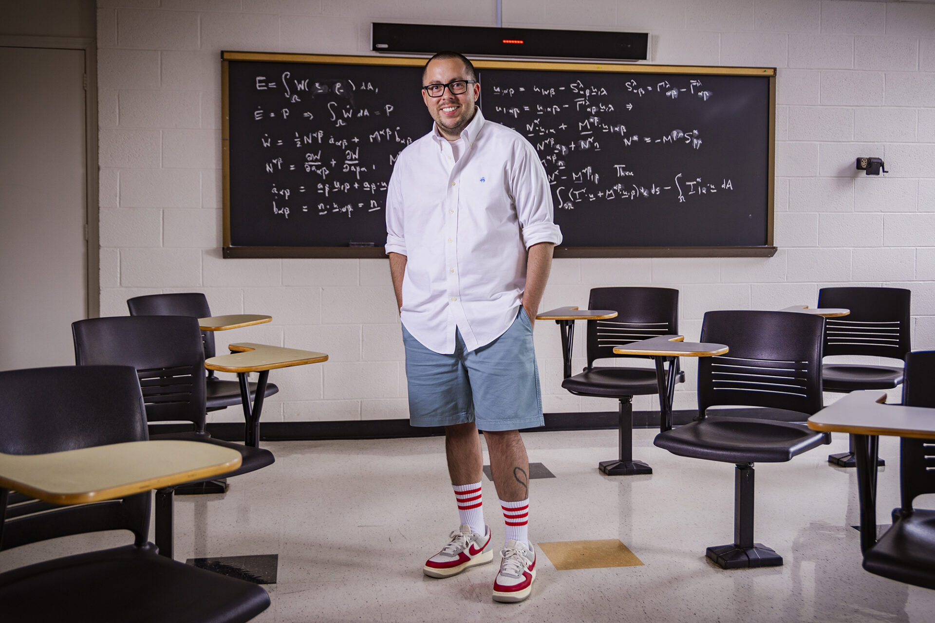 a man stands in a classroom in front of a blackboard covered in a mathematical equation