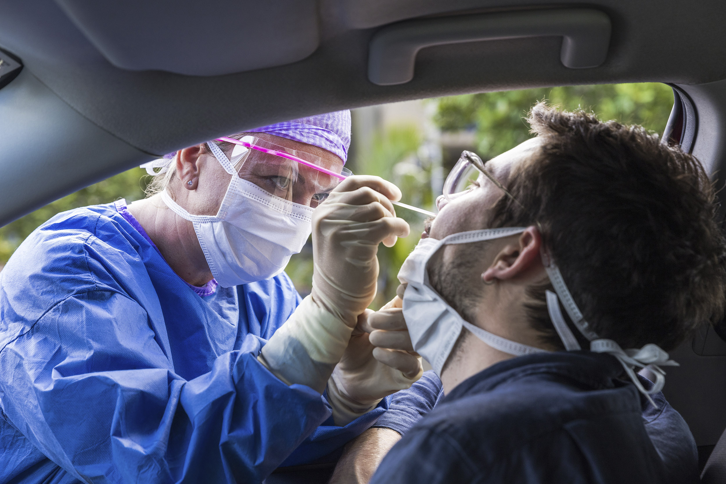 a female health care worker inserts a swab in a car passenger's nose to test for COVID-19