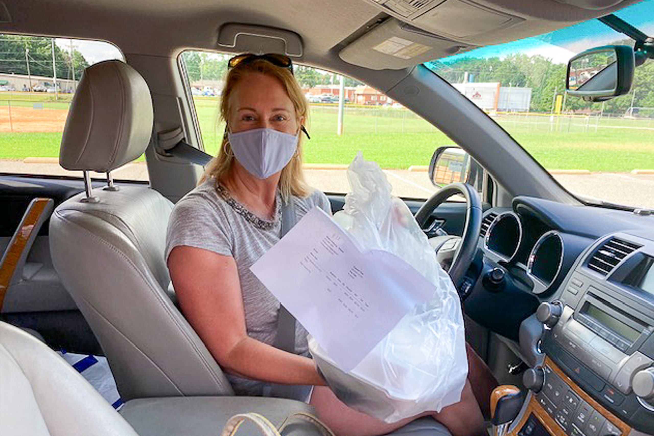 a woman wearing a mask in her car with the food she picked up from the food hub