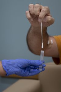 a hand placing a nasal swab into a vial