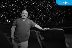  Nick Eakes standing in a planetarium theater with constellations projected on the screen above him