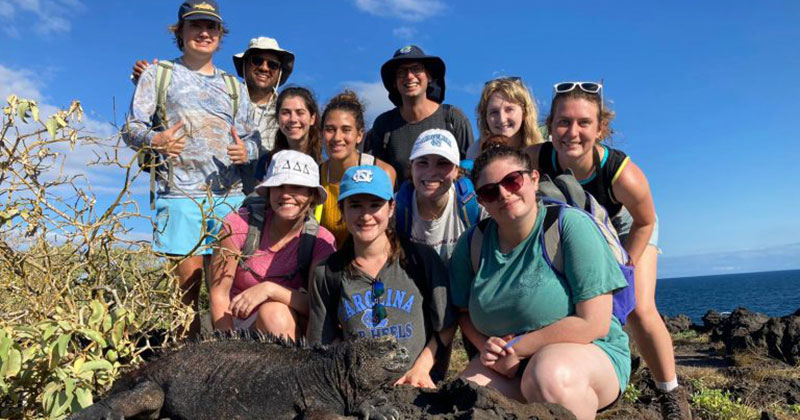 A group of college students on a tropical island gathered around a black iguana.