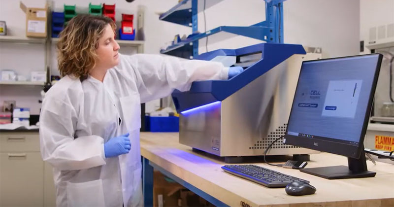 Jessica Hartman in a lab, wearing a lab coat, working with a machine.